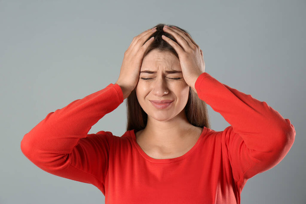Young woman suffering from migraine on grey background - Photo, Image