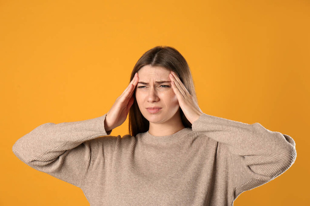 Young woman suffering from migraine on yellow background - Foto, Imagen