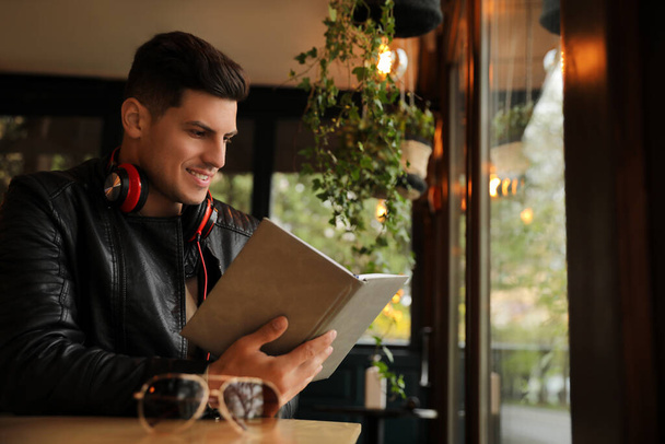 Man with headphones reading book at table in cafe - Photo, Image