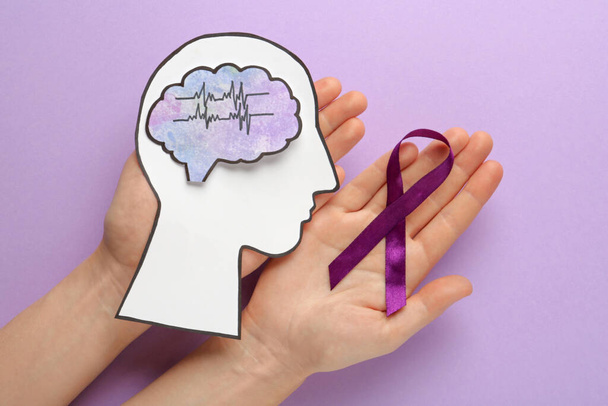 Mujer sosteniendo corte de cabeza humana, cerebro y cinta púrpura en el fondo violeta, vista superior. Concientización sobre la epilepsia - Foto, imagen