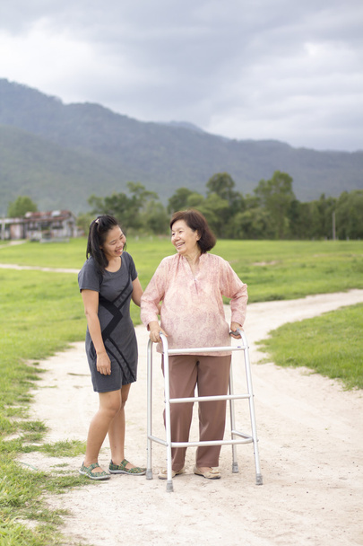 Junge Asiatin kümmert sich um Seniorin mit Rollator in Bauernhof - Foto, Bild