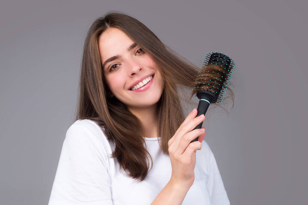 Smiling girl combing hair. Beautiful young woman holding comb straightened hair. Attractive smiling woman portrait with comb. - Foto, Imagem