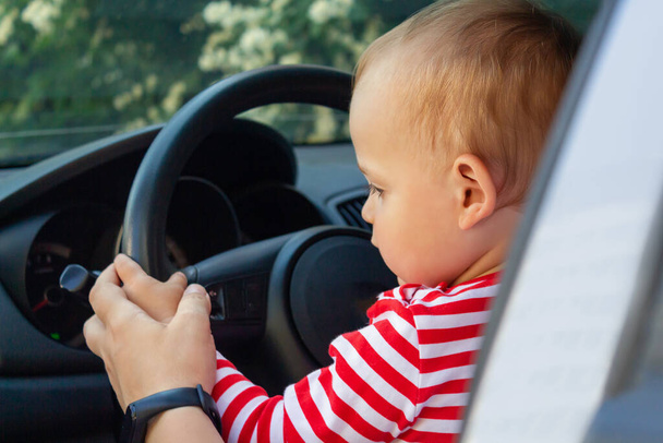 Children's hands hold the steering wheel of the car. Sitting in driver's seat in car on mom's lap. Travel with kids concept.  - Foto, imagen