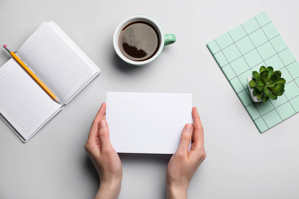 Жіночі руки з чистим аркушем паперу, чашкою кави, блокнотами та олівцем на сірому фоні
 - Фото, зображення
