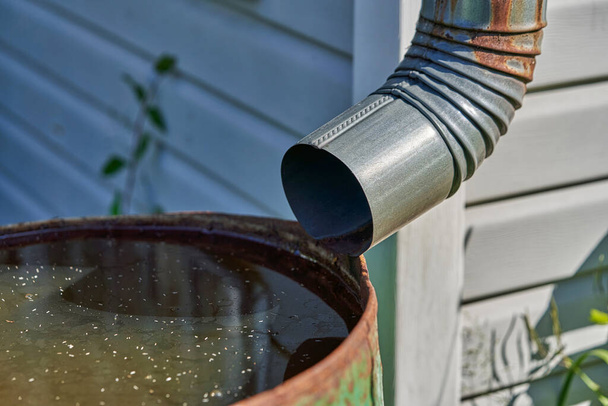 The drain pipe is connected to a rusty iron barrel with rainwater - Foto, Imagen