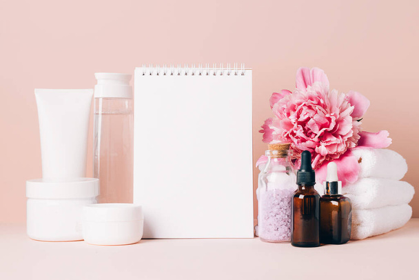 Accessoires femme crème huile divers cosmétiques nettoyer bloc-notes vierge sur une table avec des fleurs. Concept de beauté - Photo, image