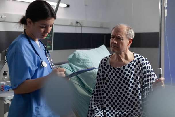 Старший хворий у лікарняній кімнаті обговорює з медсестрою
 - Фото, зображення