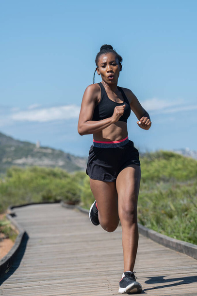 Femme afro-américaine courant rapidement le long d'une piste en bois : concept d'exercice. - Photo, image
