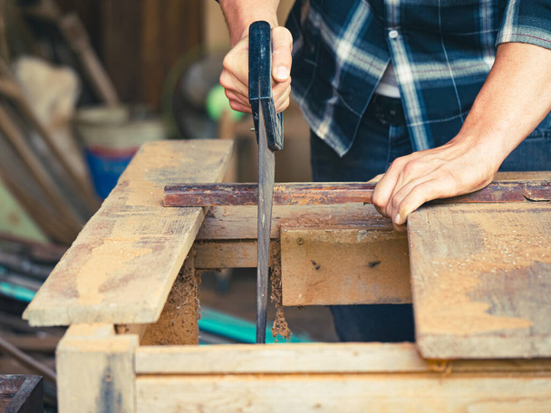 Ο ξυλουργός χρησιμοποιεί πριόνι χειρός για ξυλουργική στο εργαστήριό του. - Φωτογραφία, εικόνα