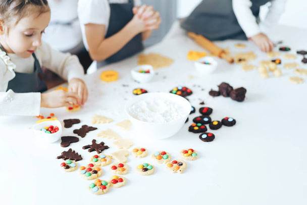 Los niños preparan galletas con dulces, un niño saca la masa con un rodillo. Actividad de ocio con concepto infantil. - Foto, imagen