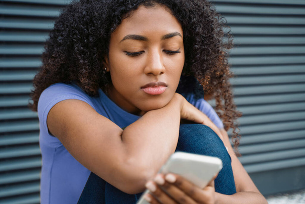 Een alleenstaande zwarte jonge vrouw met mobiele telefoon - Foto, afbeelding