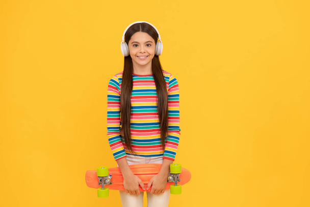 幸せなティーン女の子スケートボーダーは、ペニーボードスケートボード、子供の頃とヘッドフォンで音楽を聴く - 写真・画像