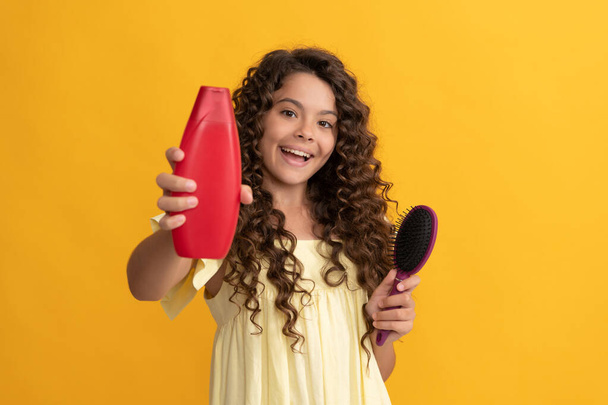 haircare and hair loss. selective focus. happy kid curly hair with comb show shampoo bottle - Photo, Image