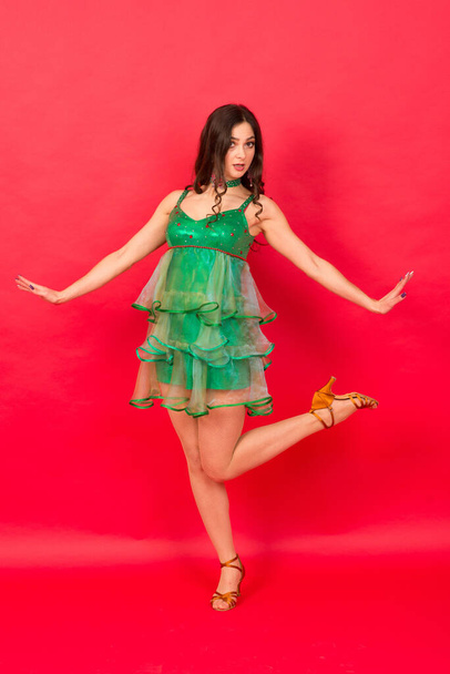 Young woman in sexy Christmas tree costume on red background in studio - Photo, Image