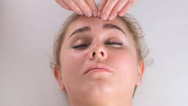 Massaggio viso trattamento di bellezza. Primo piano di una giovane donna faccia sdraiata sulla schiena, ottenere massaggio lifting facciale, pizzicare e rotolare tecnica - Foto, immagini