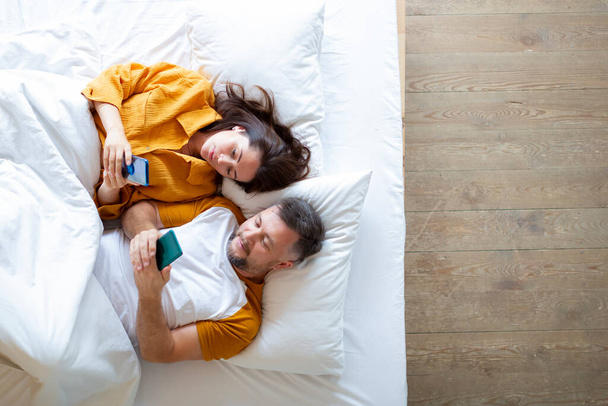 Vue du dessus du couple vivant couché au lit avec des smartphones. - Photo, image