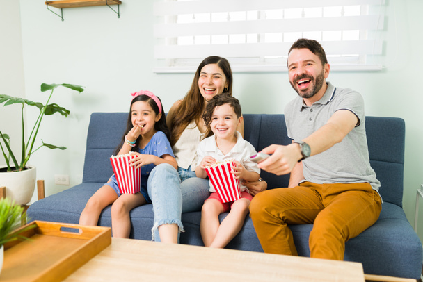 Adoriamo questo film. Bella famiglia di quattro persone che guardano un film comico insieme e ridono con snack a casa - Foto, immagini