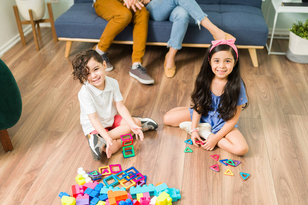 Magas szög imádnivaló kis testvérek mosolyogva, miközben a szemkontaktus és a játék szórakoztató építőkockák a nappaliban   - Fotó, kép