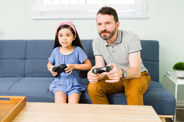 Loving hispanic dad playing video games with her cute daughter. Handsome father enjoying a fun day with her little girl  - Photo, Image