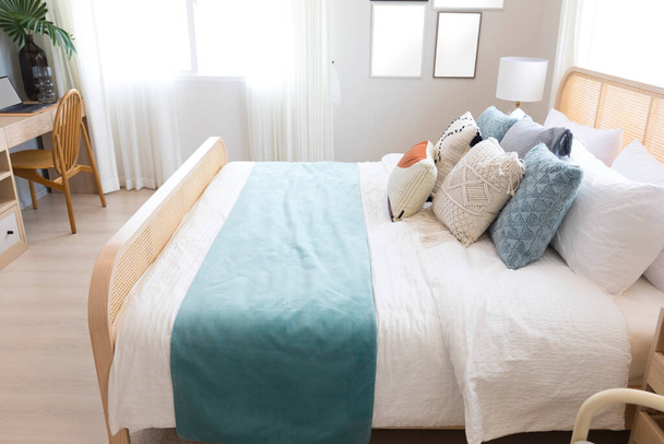 ウィッカーベッドフレーム付きの居心地の良いベッドルーム。肘掛け椅子とカーペット付きのベッドの上の緑の枕. - 写真・画像