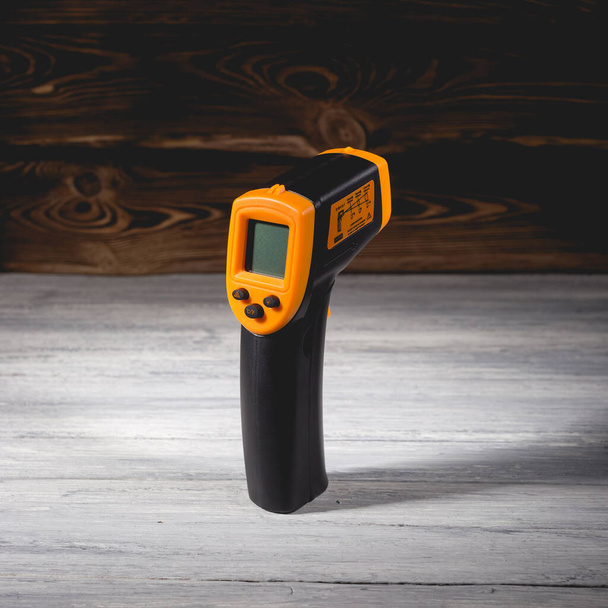 Yellow-black pyrometer on a wooden background. A device for non-contact temperature measurement. Studio photo. - Photo, Image