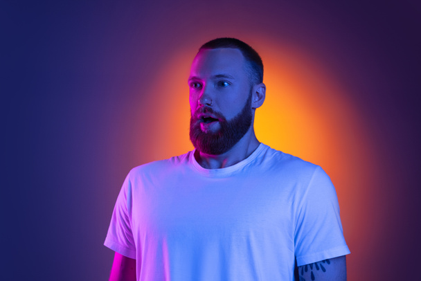 Close up portrait of young caucasian bearded man isolated on dark studio background in neon lights. Side view - Valokuva, kuva