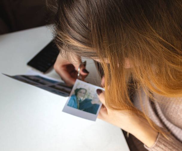 A woman cuts out photos with people in close-up. A girl uses scissors to cut printed polaroid photos for an album. A person holds a polaroid photo in his hands against the background of other photos. - Foto, Bild