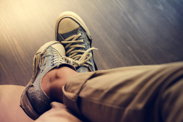  Kahverengi pantolonlu, eski mavi spor ayakkabılı bir adam kahve dükkanında oturuyor, klasik tonda. - Fotoğraf, Görsel