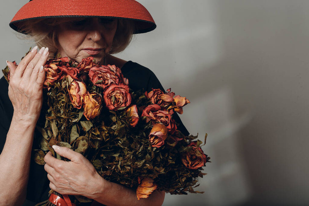 Upset elderly woman hold withered dry old rose flowers bouquet. - Foto, imagen
