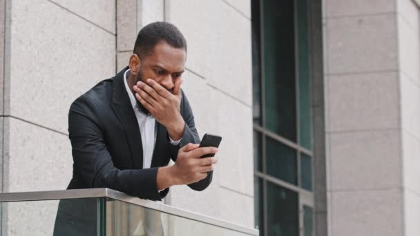 Znechucený mladý Afričan, dívající se na obrazovku chytrého telefonu, se cítil zklamaný, že dostal špatnou zprávu. Stres Smíšené rasy tisíciletý podnikatel čtení sms, otrávený bankovní oznámení o půjčce  - Záběry, video
