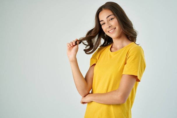 красивая брюнетка в желтой футболке держа волосы на светлом фоне - Фото, изображение