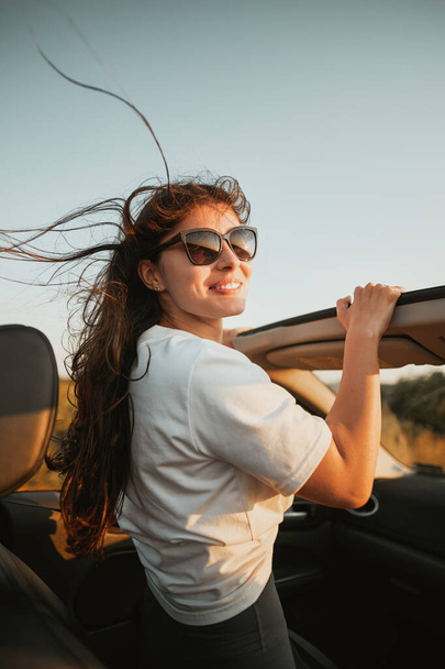 Atrakcyjna uśmiechnięta kobieta w okularach przeciwsłonecznych w kabriolecie. Pojęcie podróży letniej i przygód koleją linową. - Zdjęcie, obraz