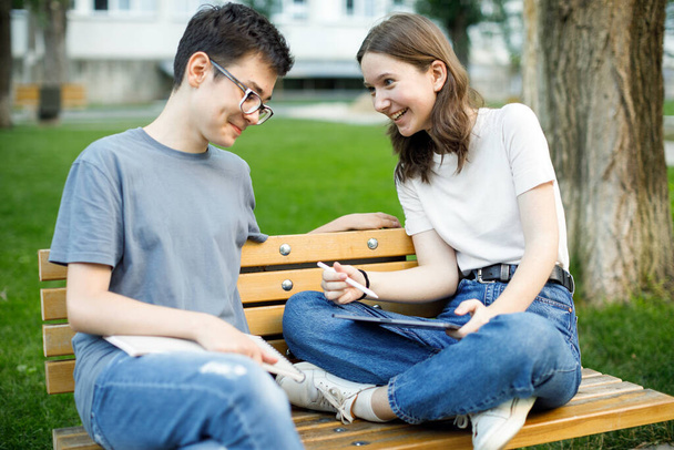 Школьные друзья разговаривают сидя на скамейке в школьном дворе - Фото, изображение