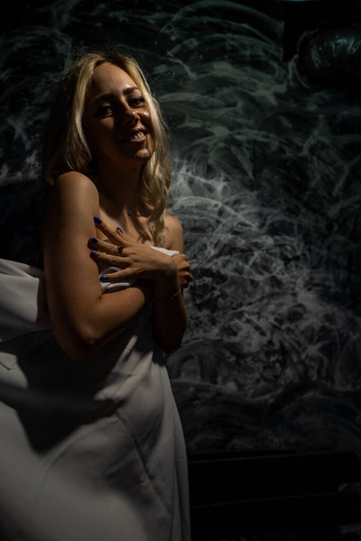Topless blonde, covered with a white cloth on a black background - Photo, Image