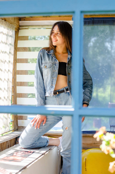 piękna młoda dziewczyna w dżinsach ubrania pozowanie w drewnianym domu w letni słoneczny dzień  - Zdjęcie, obraz
