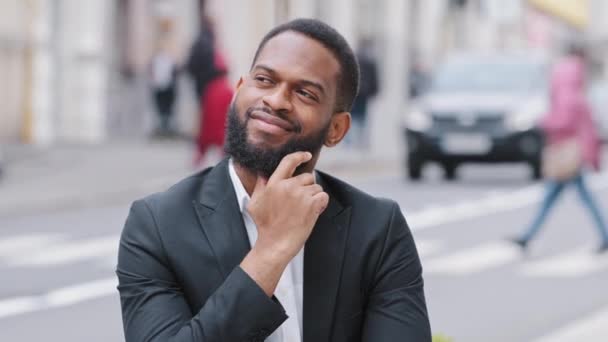 Een close-upportret van een jonge man met een baard die buiten staat. Gemengd ras student of zakenman kijkt weg na te denken over de toekomst, kiest de beste opties, analyseert, dromen. Herinneringen nostalgie in nieuwe stad - Video