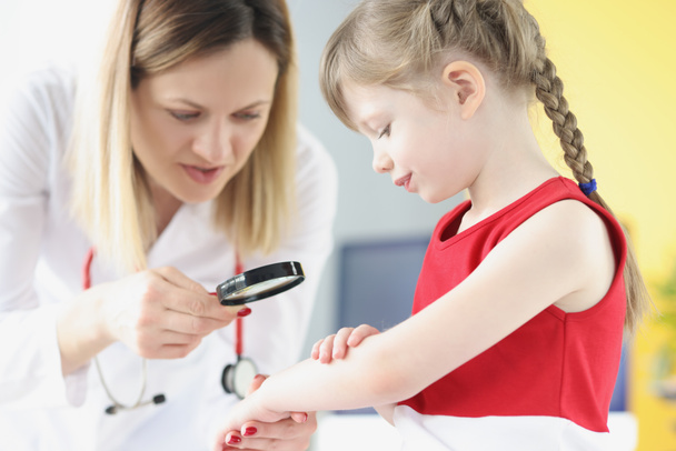 Lékař pediatr zkoumá vyrážku na kůži ruky malé dívky pomocí lupy - Fotografie, Obrázek