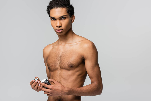 young african american man looking at camera while holding stick of antiperspirant isolated on grey - Fotografie, Obrázek