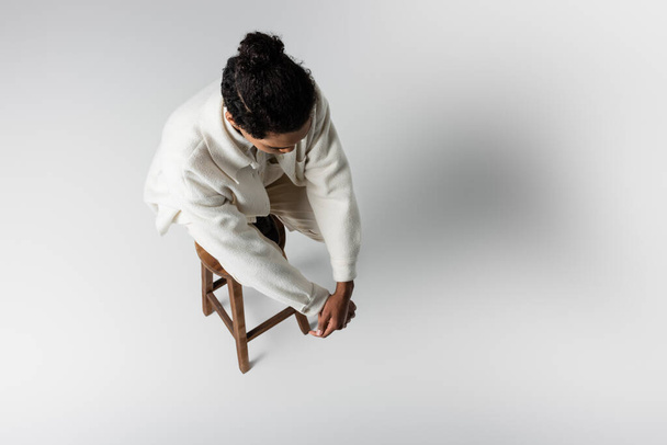 overhead view of african american guy in white clothes on high stool on grey background - Foto, Imagem