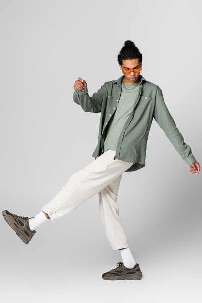 african american guy in trendy shirt and white pants posing on grey background - Foto, Imagen