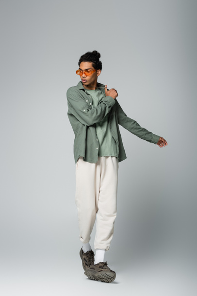full length view of african american man in shirt and white pants posing on grey background - Foto, Imagem