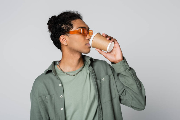 trendy african american man in shirt and orange eyeglasses drinking coffee from paper cup isolated on grey - Fotografie, Obrázek