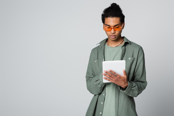 joven afroamericano hombre con elegante camisa y gafas usando tableta digital aislado en gris - Foto, imagen