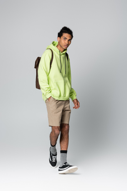 african american man in green hoodie standing with hand in pocket of beige shorts isolated on grey - Photo, Image