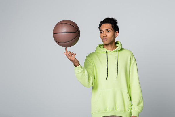 african american guy in stylish hoodie playing with basketball isolated on grey - Valokuva, kuva