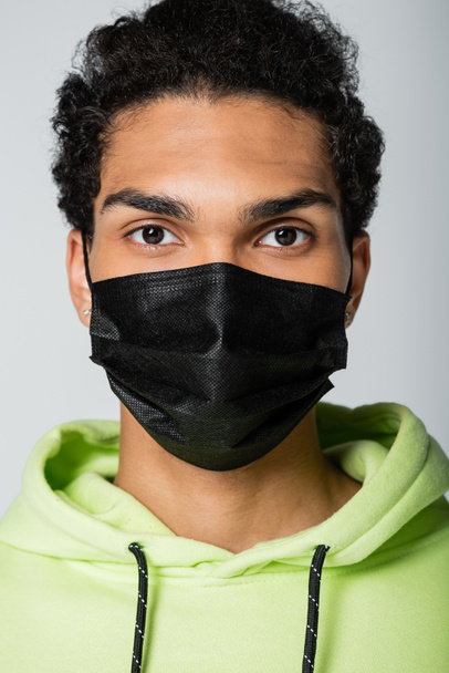 πορτρέτο του Αφροαμερικανού με τη μαύρη ιατρική μάσκα που κοιτάζει την κάμερα που είναι απομονωμένη στο γκρι - Φωτογραφία, εικόνα