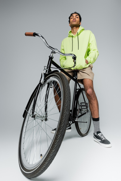 confident and stylish african american guy with bicycle looking at camera on grey background - Fotoğraf, Görsel