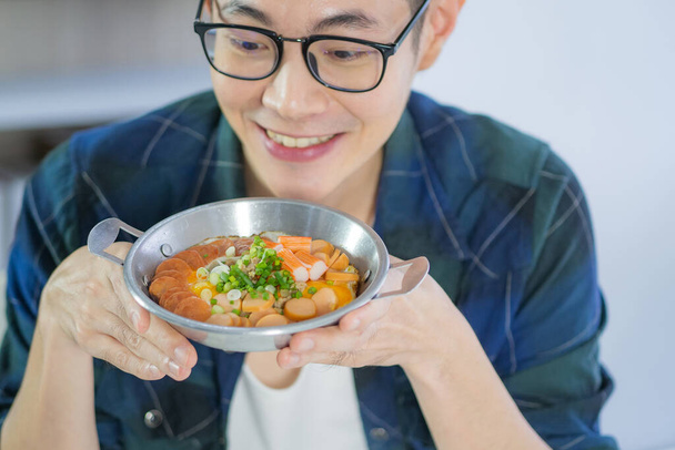 Молодой человек в очках, смотрящий на жареное яйцо с красочными начинками, подается на сковороде, сидя на стуле в кухонной комнате. Простое питание на завтрак - Фото, изображение