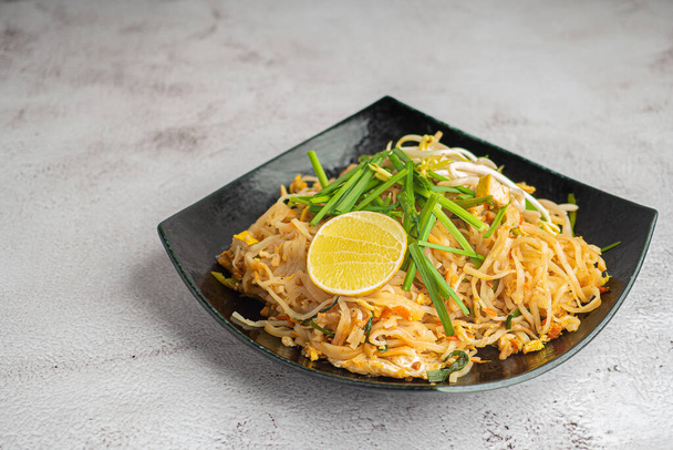 パッドタイは、灰色のセメントの背景に黒料理で野菜やレモンスライスを提供しています。タイ料理が有名。コピースペース付きのトップビュー。タイの伝統料理のコンセプト - 写真・画像