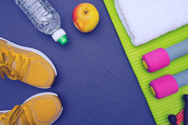 sports equipment - green mat, bottle of water and towel, sneakers and dumbbells, apple, blue, texture background - Zdjęcie, obraz